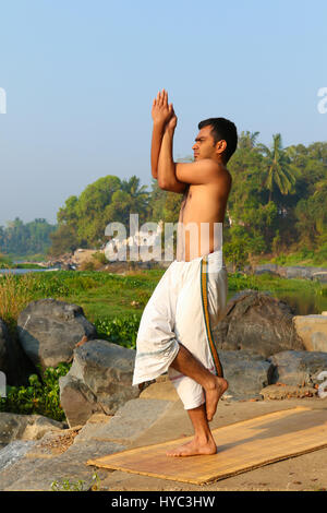 Uomo indiano a praticare yoga accanto a un fiume in India del Sud. Foto Stock