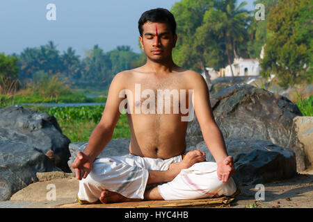 Uomo indiano a praticare yoga meditazione accanto a un fiume in India del Sud. Foto Stock