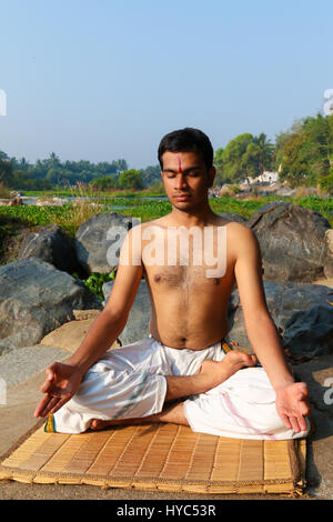 Uomo indiano a praticare yoga meditazione accanto a un fiume in India del Sud. Foto Stock