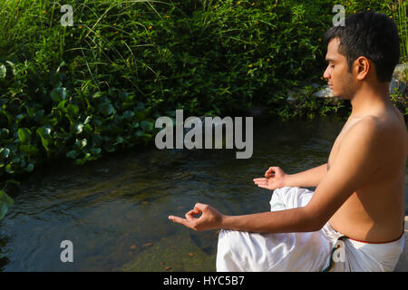 Uomo indiano a praticare yoga accanto a un fiume in India del Sud. Foto Stock