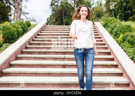 Felice giovane donna in maglia bianca di discesa delle scale in posizione di parcheggio Foto Stock