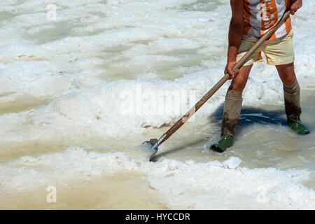 Lavoratore shoveled il sale cristallizza al di fuori del terreno nel sale farm , riempito con sale naturale dal mare. Trapani, Italia Foto Stock