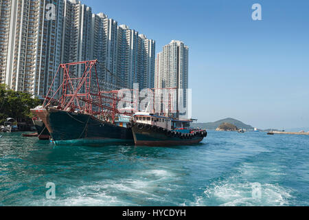 Commerciale barche da pesca ormeggiate nel canale di Aberdeen, alta edifici di appartamenti su Ap Lei Chau isola dietro. Hong Kong. Foto Stock