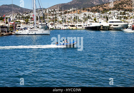 Zodiac passa e va in Bodrum marina. Molti yacht di lusso e Bodrum cityscape sono nella vista. È una soleggiata giornata estiva. Foto Stock