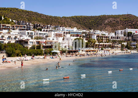 Persone di nuotare in spiaggia Icmeler vicino al centro cittadino di Bodrum. È una soleggiata giornata estiva. Tradizionale, bianco, tipica estate case riflettono della regione dell'architettura Foto Stock