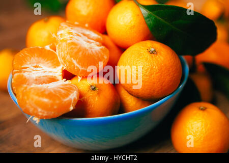 Molti freschi mandarini arance in blu ciotola, in piedi su un tavolo di legno Foto Stock