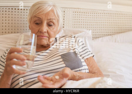 Senior infelice donna giaceva a letto assunzione di medicina Foto Stock