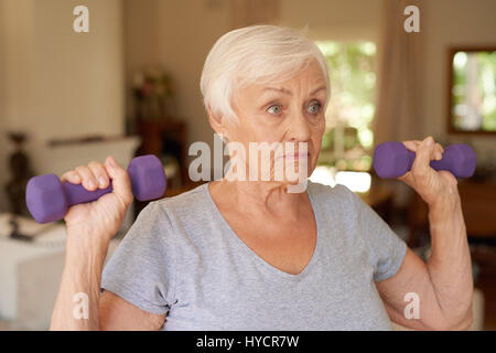 Attiva donna senior focalizzata sul sollevamento manubri a casa Foto Stock