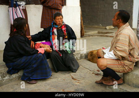 Il Bhutan la popolazione locale in stoffa tradizionale chat sul Boardwalk e masticare Moma e spiti sul terreno, Paro, Bhutan Foto Stock