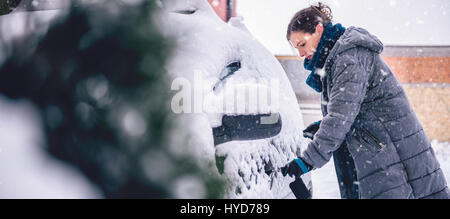 Donna che indossa grigio giacca invernale e a mano in pelle Guanti neve di sblocco auto coperto Foto Stock