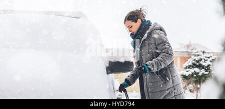 Donna che indossa grigio giacca invernale e a mano in pelle Guanti neve di sblocco auto coperto Foto Stock