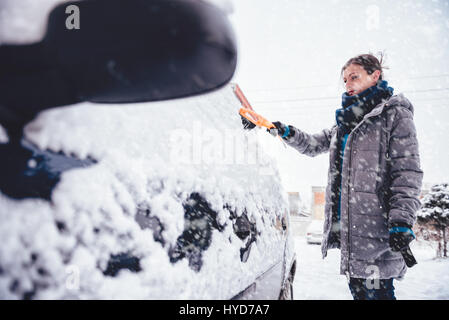 Donna che indossa grigio giacca invernale e in pelle Guanti a mano e rimuovere la neve da auto con spazzola di neve Foto Stock