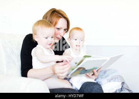 Madre e figli (12-17 mesi) leggendo un libro di immagini Foto Stock