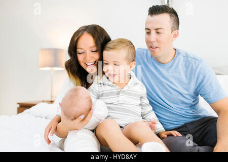 Genitori seduti con la figlia (0-1 mesi) e figlio (4-5) sul letto in camera da letto Foto Stock
