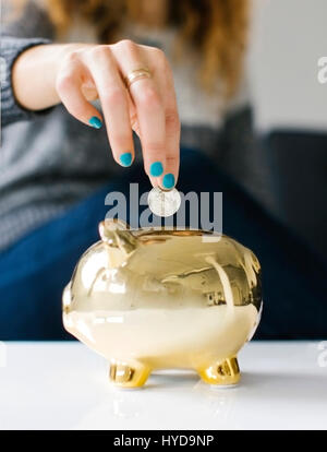 Donna che cade moneta in oro piggy banca Foto Stock