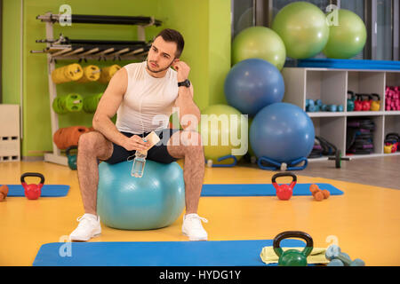 Uomo seduto su una palla in possesso di un telefono cellulare dopo aver fatto un lavoro fuori Foto Stock