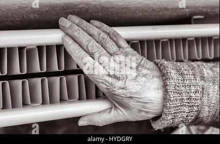 90 anni di donna con la mano sul radiatore. Regno Unito Foto Stock