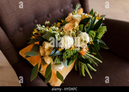 Bouquet nuziale. La sposa il bouquet. Bel bouquet di peonie bianco, crema di rose e verde, decorato con seta arancione nastro, giace sul oran Foto Stock