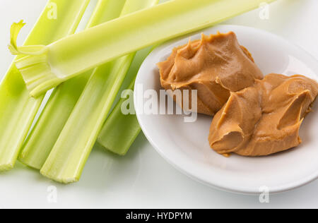 Vista ravvicinata di gambi di sedano con una tazza di burro di arachidi su una piastra bianca. Foto Stock