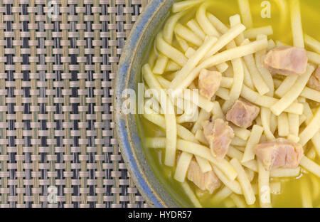 Top vista ravvicinata di una zuppa di noodle al pollo in un vecchio recipiente di ceramica sulla cima di un tessuto di plastica posto mat. Foto Stock