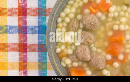 Top vista ravvicinata di un recipiente di ceramica riempito con stile Italiano zuppa di nozze sulla cima di un panno colorato posto mat. Foto Stock