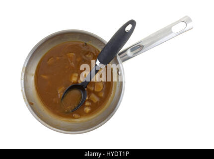 Vista dall'alto di avanzi di bistecca e patate stufato di carne in una padella di acciaio con un cucchiaio di nero nel cibo isolato su uno sfondo bianco. Foto Stock