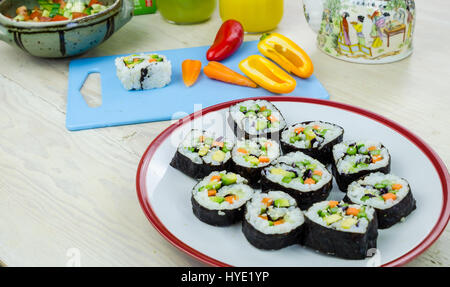 Fatto in casa sushi vegano rotola su una piastra e le verdure su una scheda blu Foto Stock