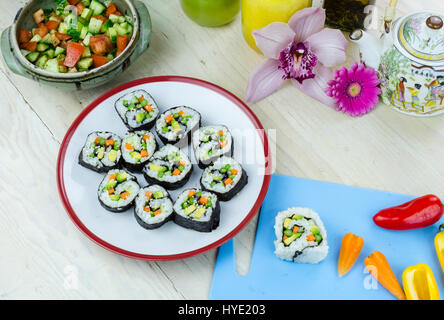 Fatto in casa sushi vegano rotola su una piastra e le verdure su una scheda blu Foto Stock