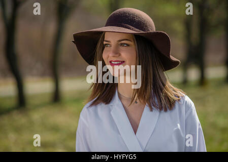 Ritratto di un sorridente giovane donna che indossa un cappello in un parco durante la primavera. La donna piegò la sua testa testa sul lato destro del telaio. Medium Shot. De poco profonda Foto Stock