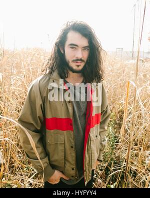 Giovane uomo con la barba e capelli lunghi guarda nella fotocamera in un campo oro Foto Stock