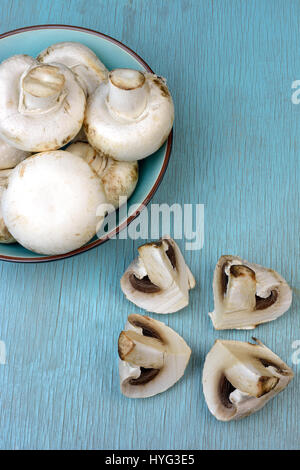 Agaricus bisporus di funghi in ciotola sul blu turchese tabella Foto Stock