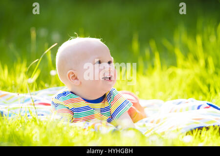 Adorable baby boy eating apple giocando sul manto colorato in verde erba. Bambino divertirsi sulla famiglia picnic nel giardino estivo. I bambini mangiano la frutta. Un sano Foto Stock