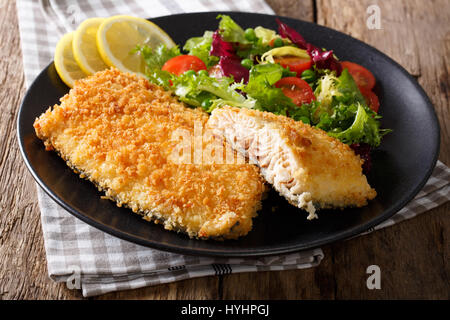 Gustoso arrosto di filetto di pesce nel pangrattato e verdure fresche close-up su una piastra orizzontale. Foto Stock