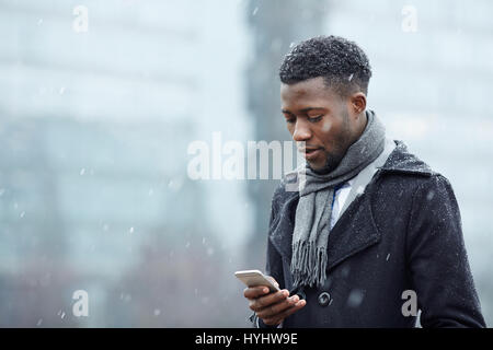 Bello l'uomo africano con lo smartphone nella neve Foto Stock