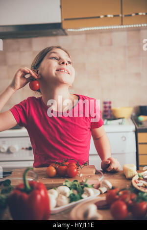 Carino bambina ingannare intorno con il pomodoro in cucina Foto Stock