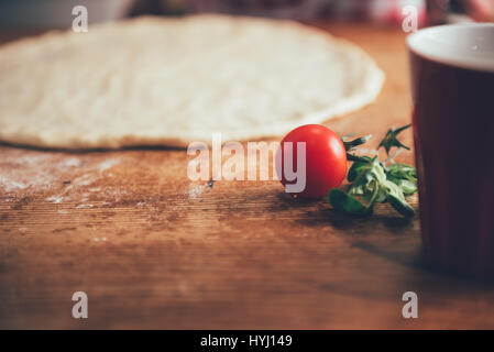 Impasto per pizza e pomodoro ciliegino sul tavolo di legno Foto Stock