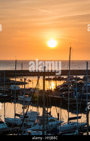 Inghilterra, Ramsgate. Tramonto sul mare e il porto di Marina yachting. Sun salito al di sopra di orizzonte, in cielo arancione. Sagome dei montanti e delle barche in Marina yachting. Close up. Foto Stock