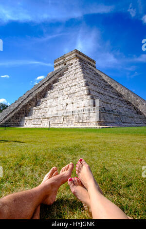 Pyramid Castillo a Chichen Itza e le gambe della coppia relax su erba, Messico Foto Stock