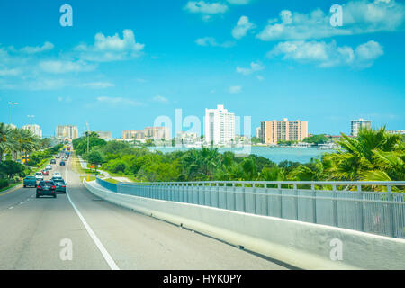 Viaggiano in Clearwater Memorial Causeway, entrando in Clearwater Beach, FL sul Golfo del Messico con edifici distanti e cintura verde Foto Stock