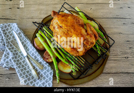 Deliziosa dorate e croccanti della pelle di pollo grigliato in forno con spicchi di patate e porri in ghisa pan su vecchie tavole di legno, vista da sopra Foto Stock