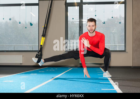 Ricci bianco barbuto uomo sportivo esercitando con cinghie di fitness in palestra Foto Stock