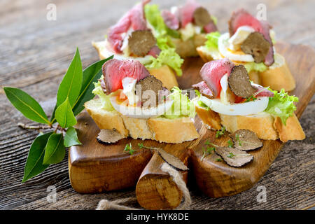 Crostini con roast beef , nero tartufo d'autunno, Francese Formaggio Brie su una fetta di uovo sulla baguette con una foglia di insalata Foto Stock