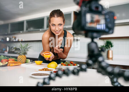 Giovane donna la registrazione di alimenti a base di contenuti video sulla fotocamera. La donna rivolta verso un taglio arancione rivolta verso la telecamera. Foto Stock