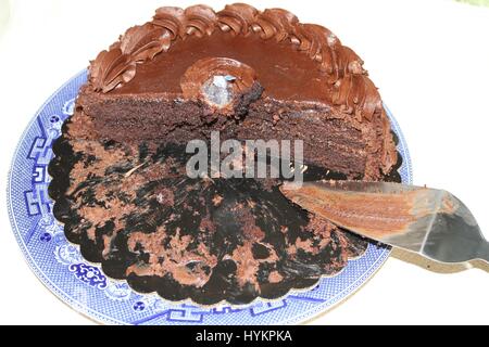 Un round dolce torta al cioccolato con crema di colore marrone su un grande blu e bianca porcellana piatto. La metà della torta e Server la torta su un piatto da portata. Torta di vacanza. Foto Stock