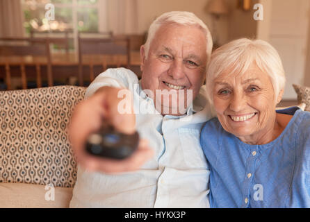 Sorridente coppia senior cambiando i canali televisivi con un telecomando Foto Stock