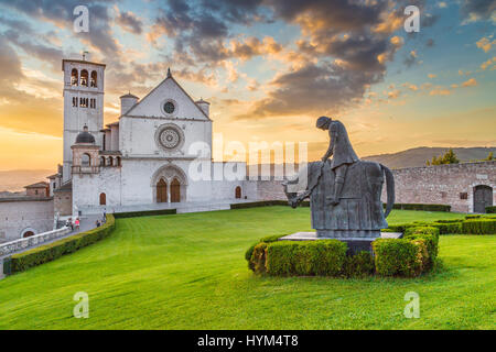 Visualizzazione classica della famosa Basilica di San Francesco di Assisi (Basilica Papale di San Francesco) con statua in beautiful Golden luce della sera con dramati Foto Stock