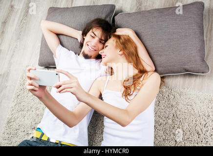 Felice coppia giovane prendendo un selfie sul pavimento a casa Foto Stock