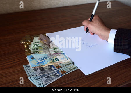 Braccio della persona d'affari nella camicia tenendo una penna con euro, in lire e in dollari USA sul tavolo accanto alla nota la carta Foto Stock