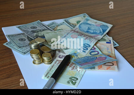 Monete di carta, Lire, dollari, euro lungo con monete e penna su bianco nota carta su una scrivania in legno Foto Stock