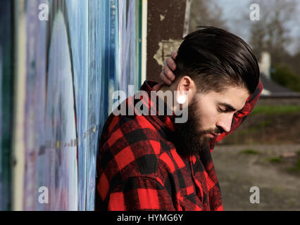 Vista laterale verticale di un giovane uomo con la barba e piercing all'aperto Foto Stock